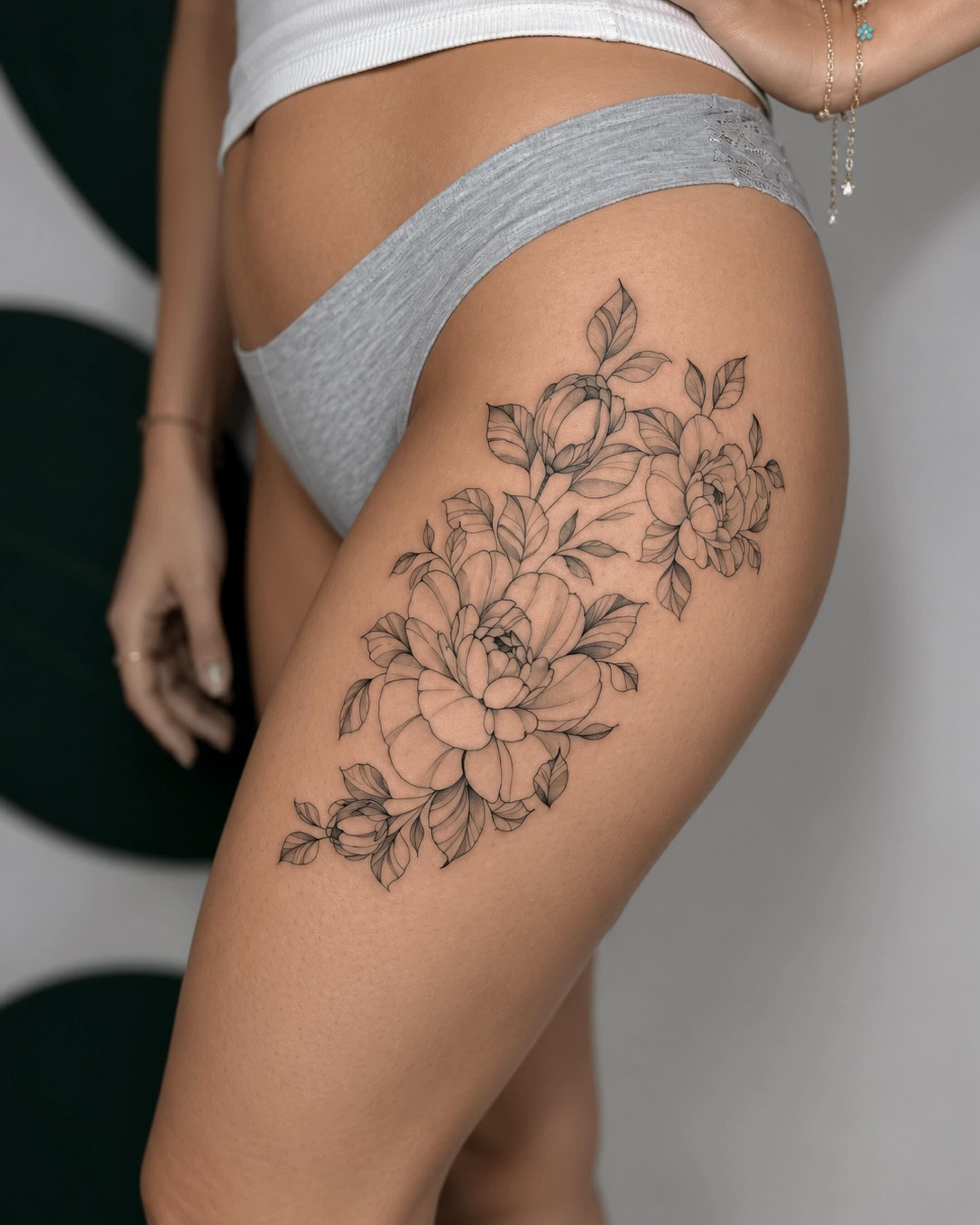 Fine line floral thigh tattoo with peony and leaves