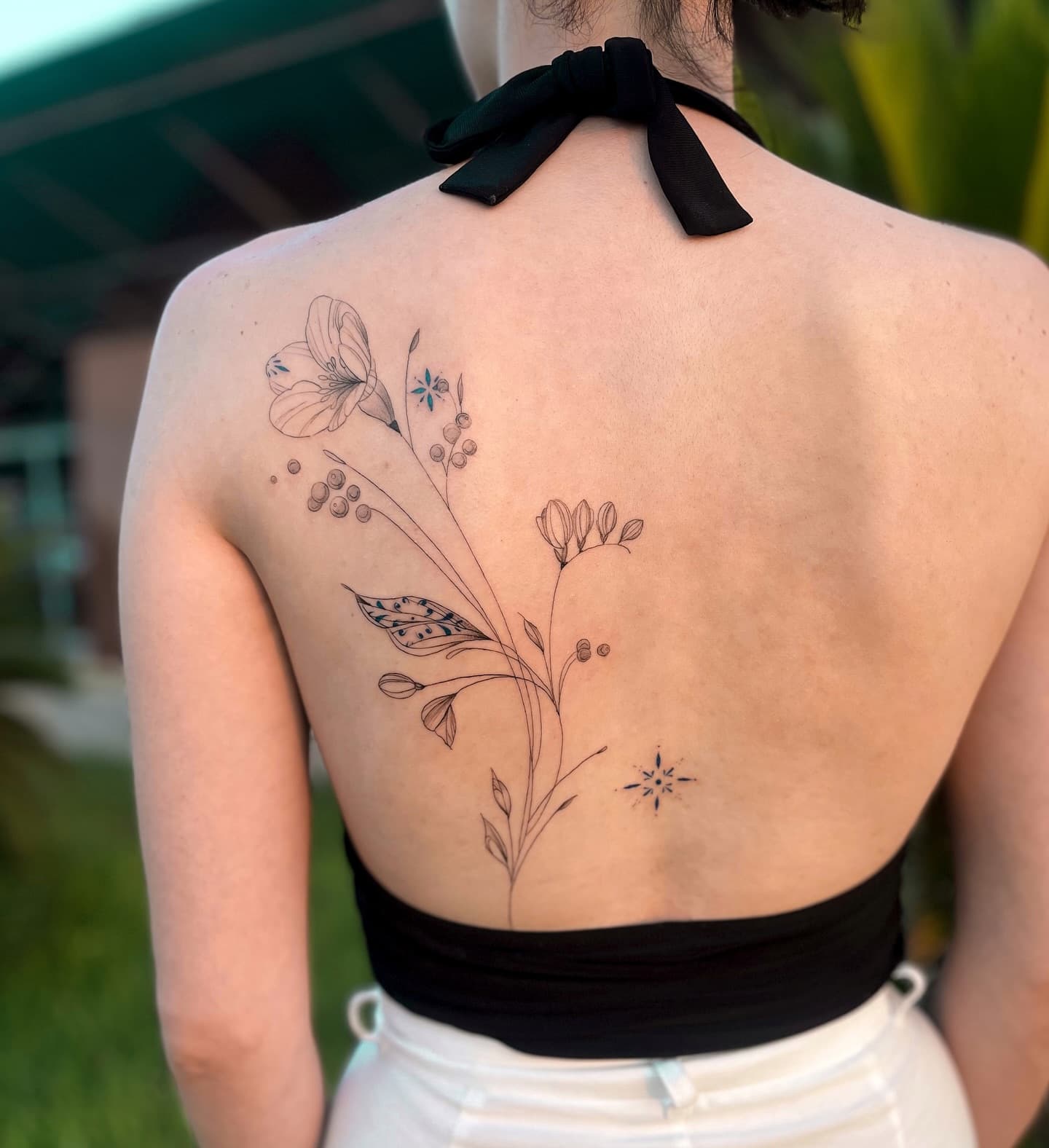 Fine line floral back tattoo with blue accents